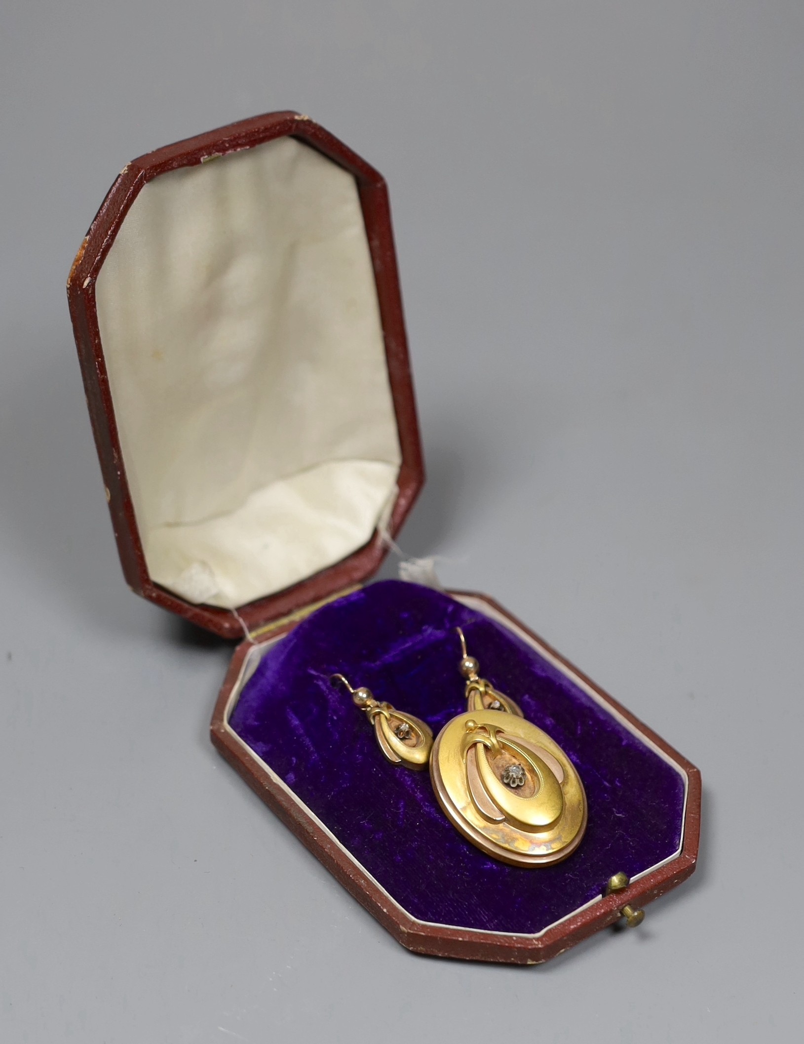 A Victorian 15ct two colour gold and diamond set pendant brooch, of oval form with central stylised motif, 3.5cm, in fitted case with a pair of matching earrings, gross 10.2 grams